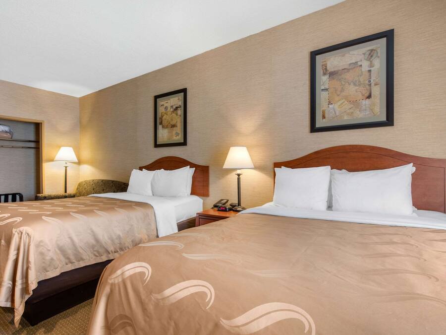 A hotel room with two beds, each with a wooden headboard, a nightstand with a lamp, and a framed map on the wall.