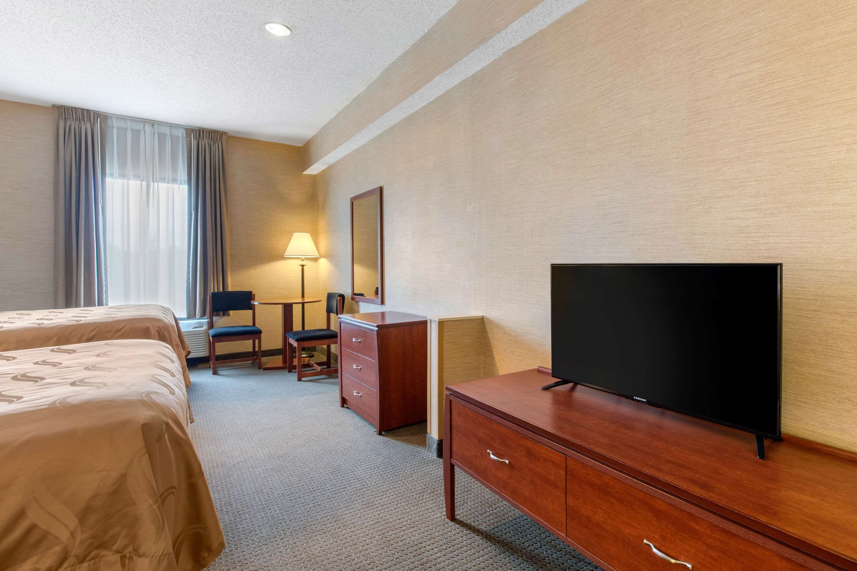 A hotel room with two beds, a desk, a chair, a television, and a lamp.