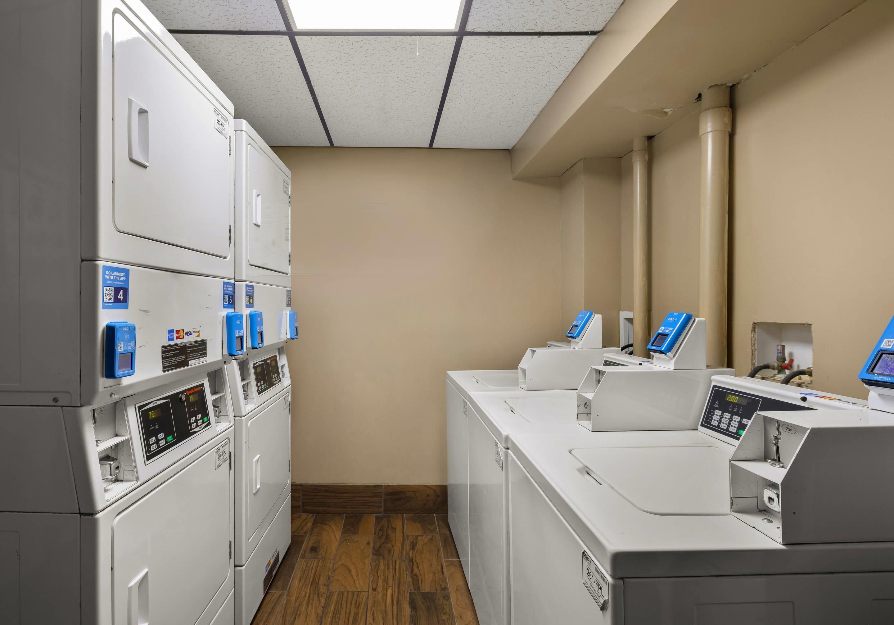 A laundry facility with multiple washing machines and dryers, control panels, and a ventilation system.