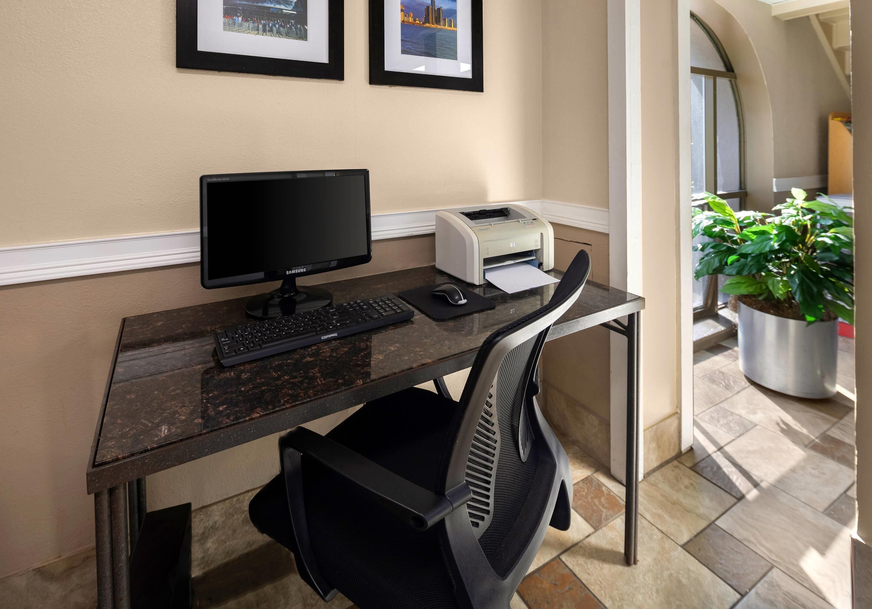 Un bureau avec un ordinateur, un clavier et une imprimante, une chaise, et des tableaux encadrés accrochés au mur.