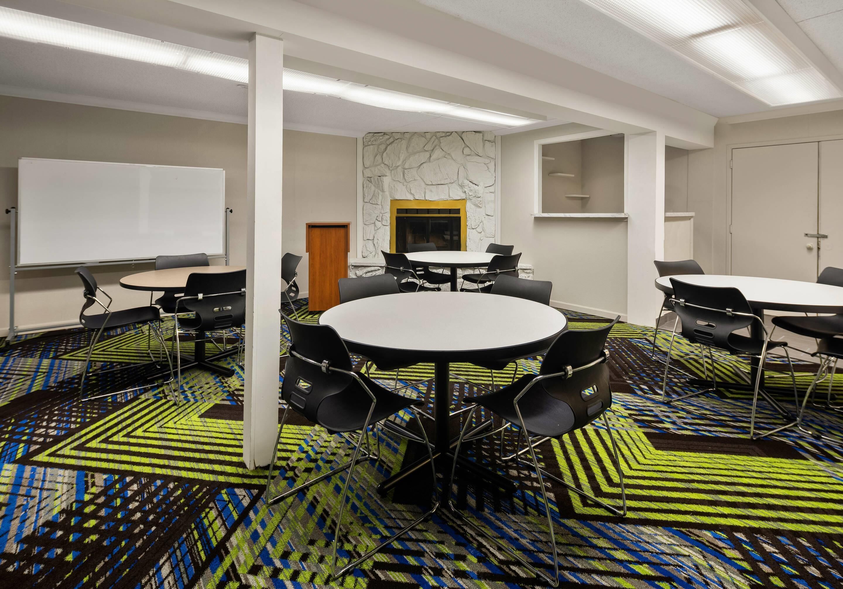 Uma sala de conferências com quadro branco, várias mesas e cadeiras.