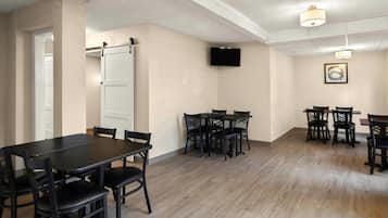 A conference room with a large table and chairs, a television mounted on the wall, and a framed picture.
