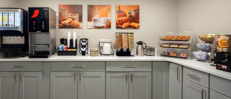 Una kitchenette con cafetera, dispensador de bebidas y una selección de pasteles.
