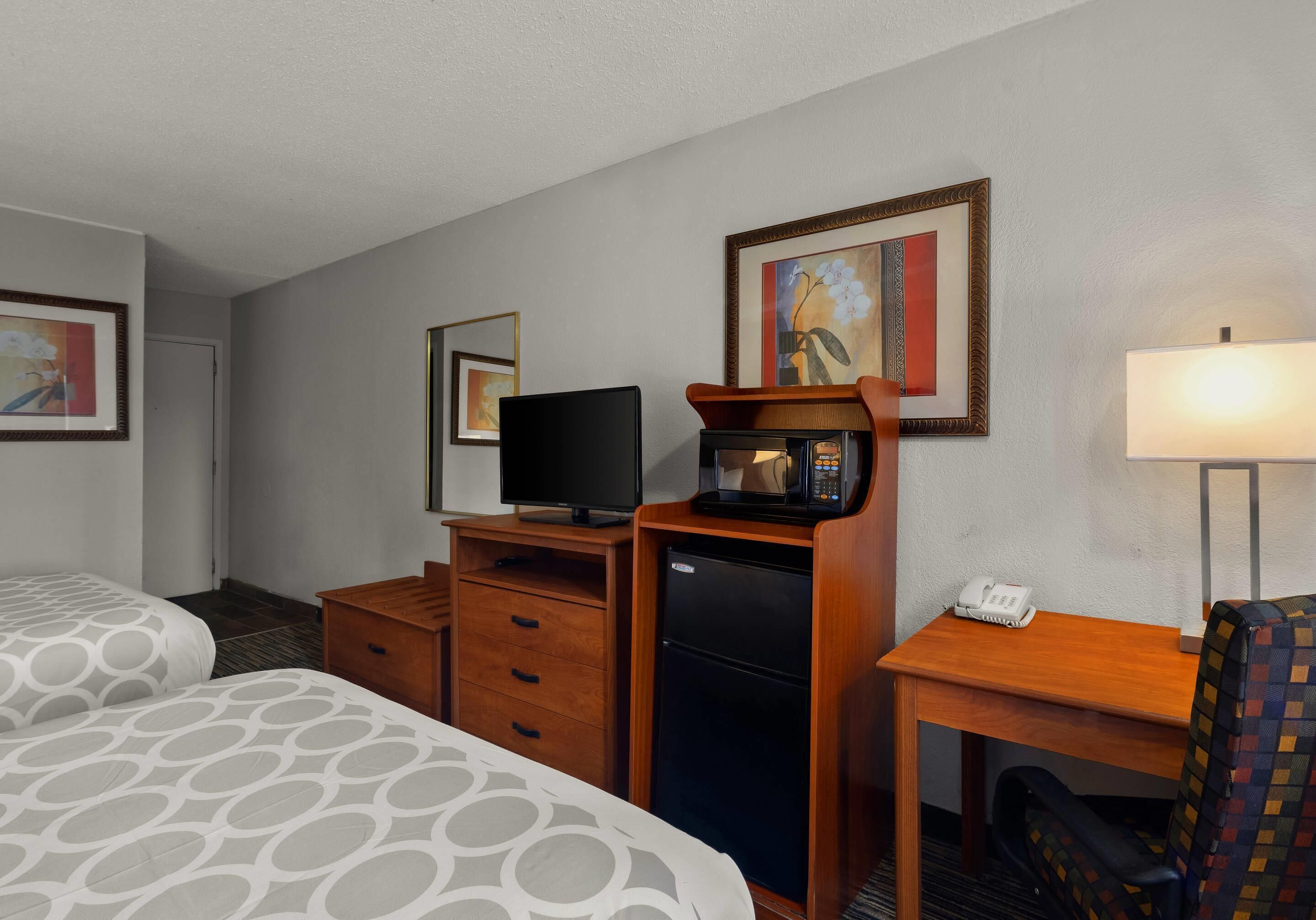 A hotel room with a bed, a desk with a telephone, a microwave, a television, and a refrigerator.