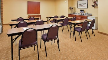 Un salón de conferencias con mesas y sillas, una kitchenette y un cuadro en la pared.
