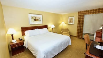 A hotel room with a bed, two bedside lamps, a chair, a desk with a computer, and two framed pictures on the wall.
