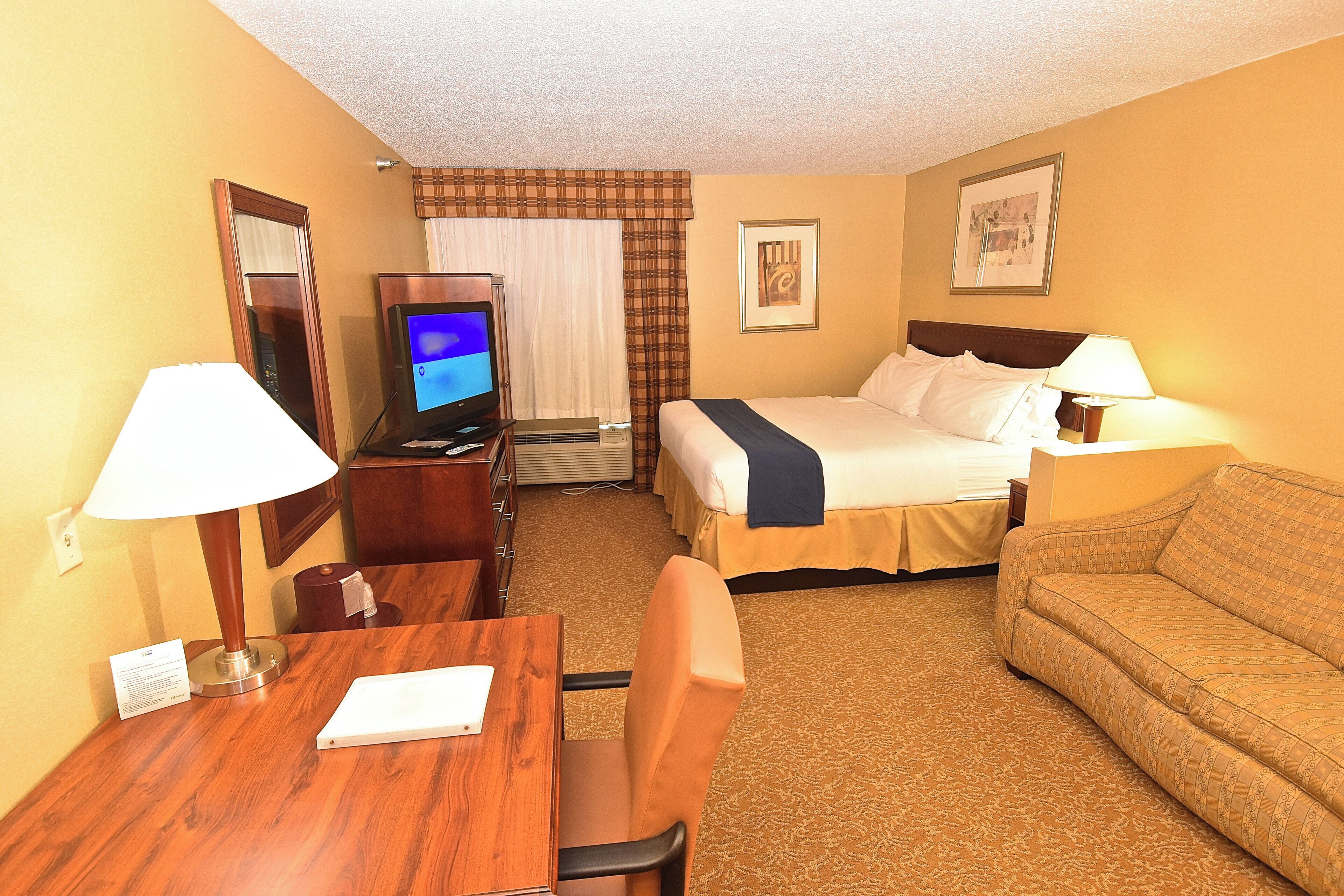 A hotel room with a bed, a desk with a chair, a television, a sofa, and a lamp.