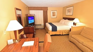A hotel room with a bed, a desk with a chair, a television, a sofa, and a lamp.