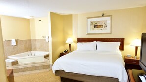 Une chambre d’hôtel avec un grand lit, une salle de bain séparée avec une baignoire, un téléviseur à écran plat et un tableau encadré au mur.