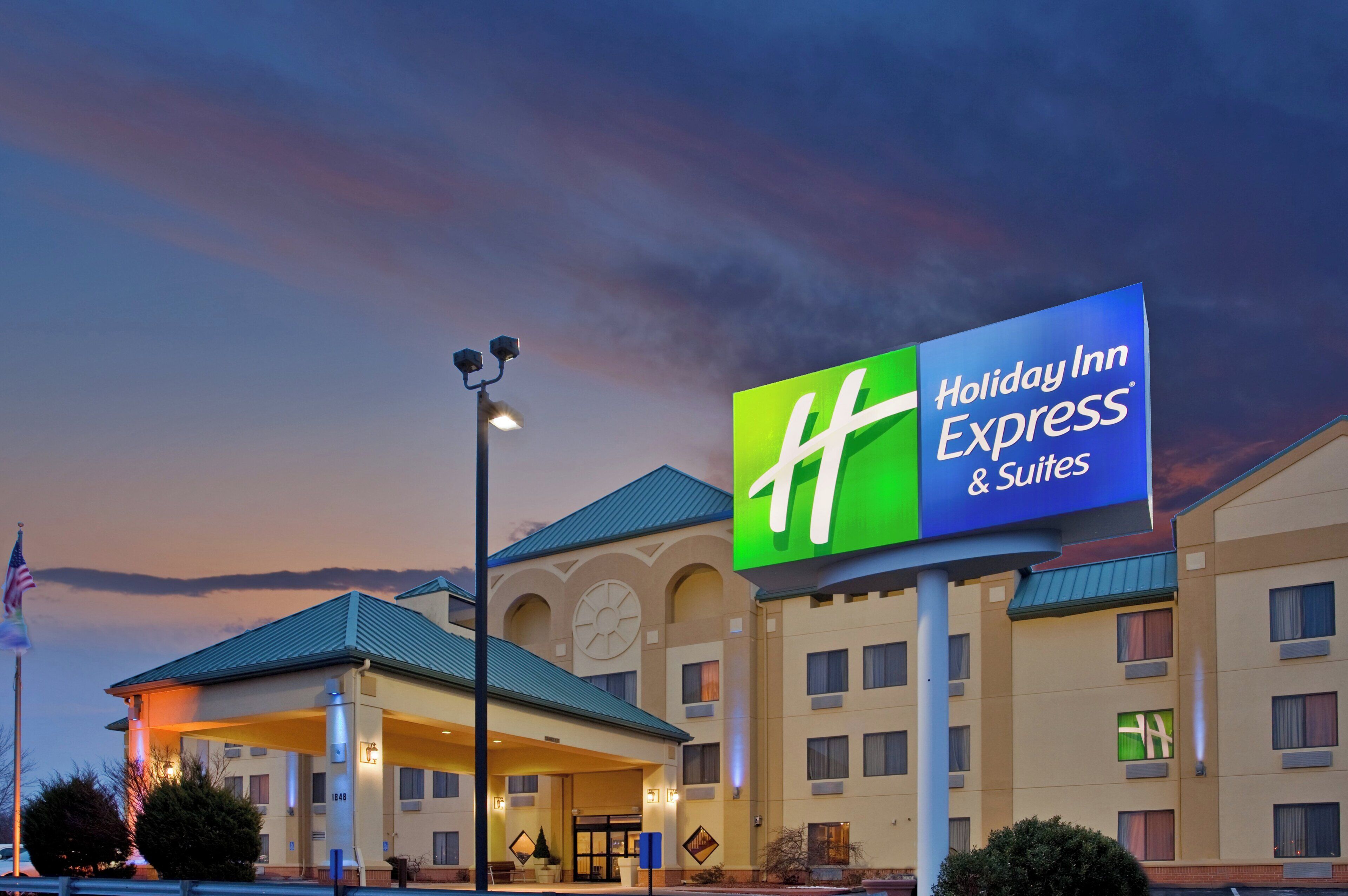 A Holiday Inn Express & Suites building with a prominent sign, a flag, and a well-lit entrance.