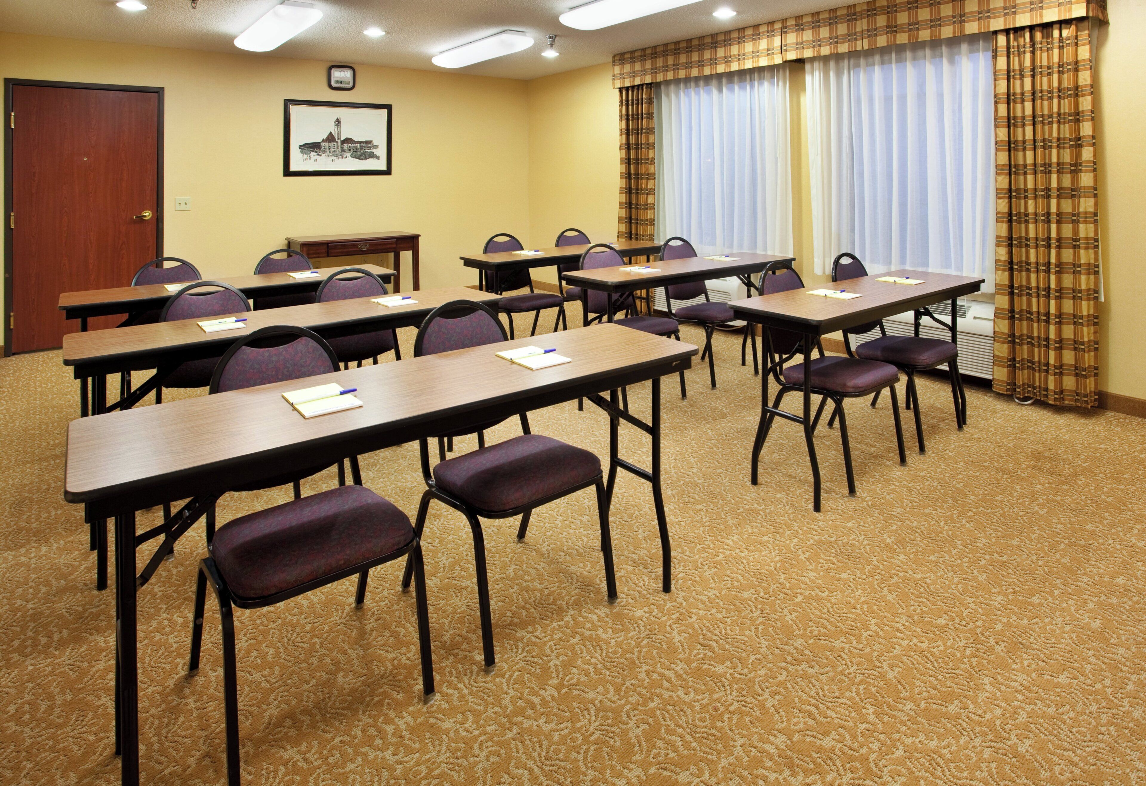 A conference room with multiple tables and chairs, carpeted floor, and a door in the background.