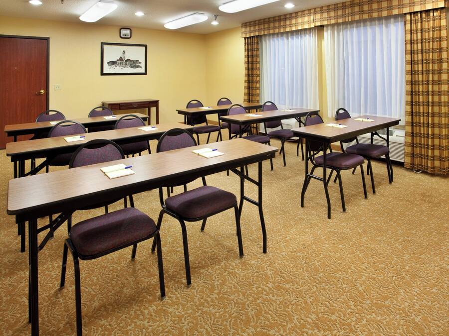 Ein Konferenzraum mit mehreren Tischen und Stühlen, einem Teppichboden und einer Tür im Hintergrund.