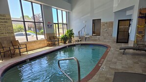 Une piscine intérieure avec un sol carrelé, un escalier pour entrer dans la piscine, ainsi que quelques chaises et tables disposées autour de la piscine.