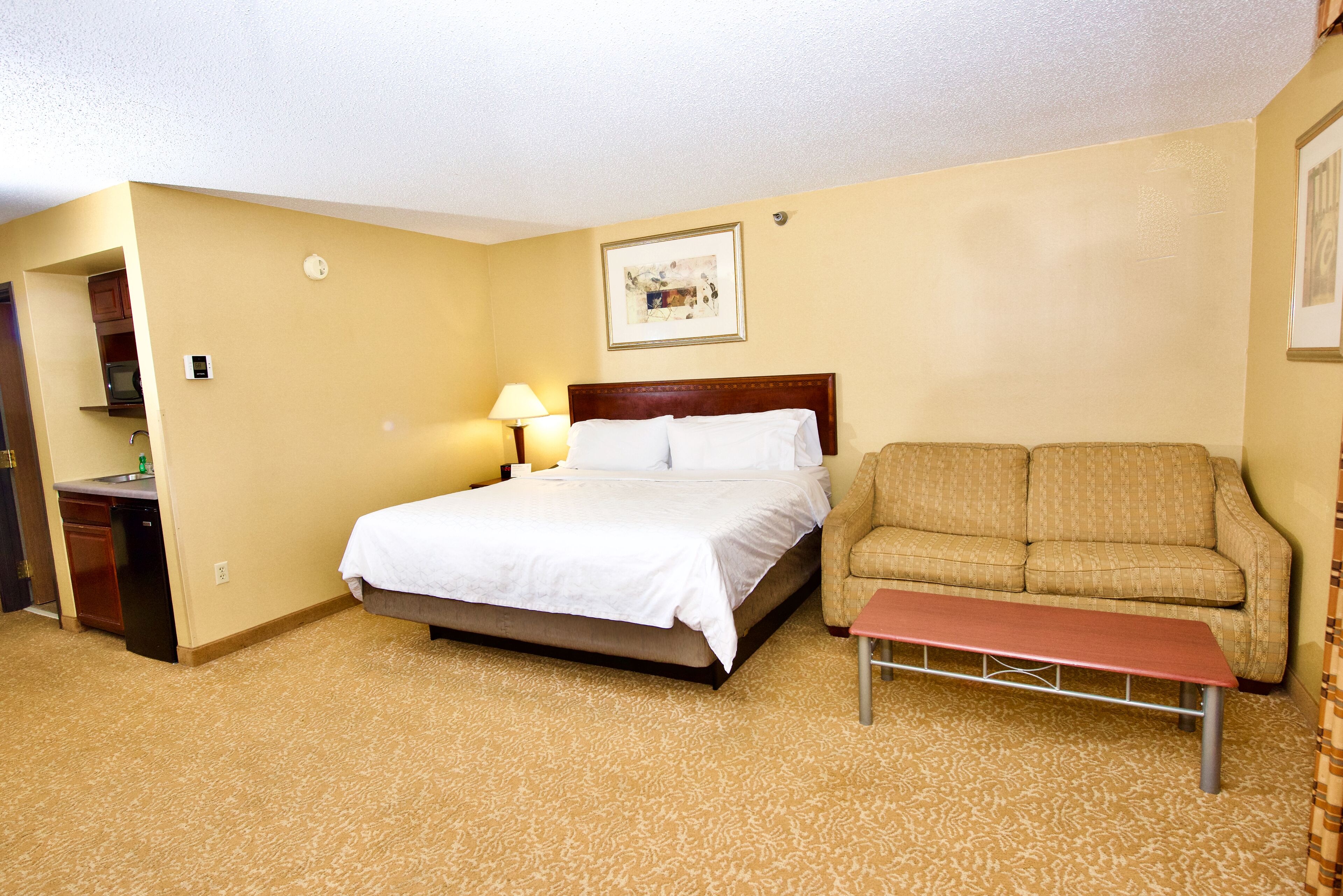 A hotel room with a bed, a sofa, a small table, and a lamp.