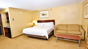 A hotel room with a bed, a sofa, a small table, and a lamp.