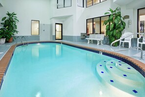 An indoor swimming pool with a clear water surface, surrounded by a tiled edge. There are potted plants, a bench, and a chair near the pool. - Holiday Inn Express & Suites St. Louis West - Fenton by IHG (Fenton)