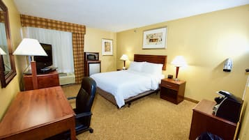 Una habitación de hotel con una cama, dos mesitas de noche con lámparas, un escritorio con una silla, un televisor, un microondas y un cubo de basura.