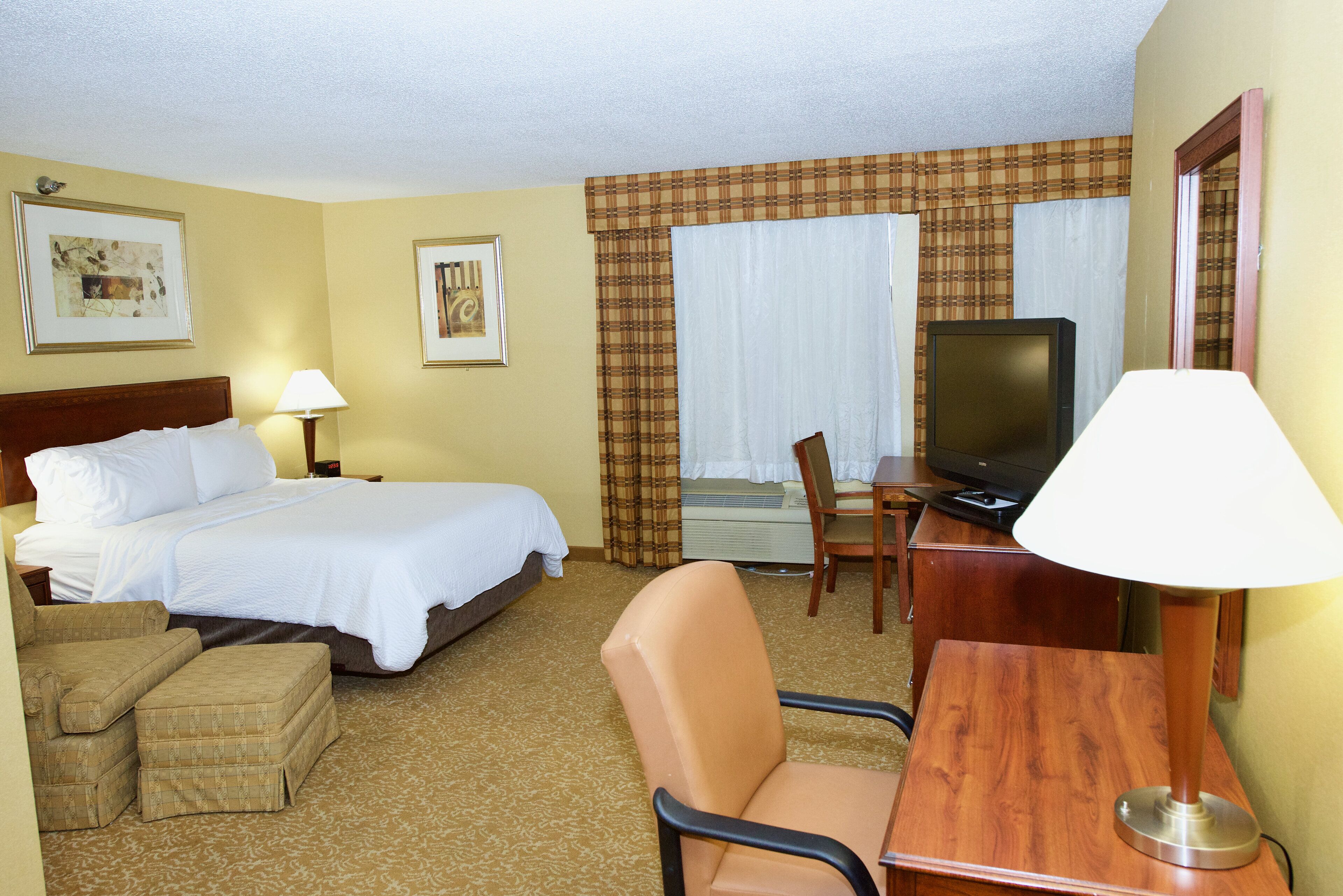 Una habitación de hotel con una cama, un escritorio con televisor, una silla y una lámpara.