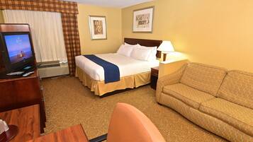 A hotel room with a bed, a sofa, a desk with a computer, and a TV displaying a beach scene.