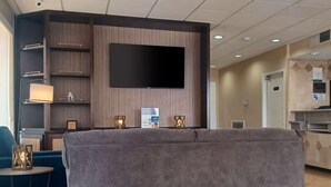 Un hall d’hôtel doté d’un téléviseur à écran plat fixé sur un mur en bois, d’un canapé, d’une petite table avec une lampe et de lanternes décoratives.