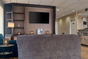 Um saguão de hotel com uma TV de tela plana fixada em uma parede de madeira, um sofá, uma mesa pequena com abajur e lanternas decorativas.
