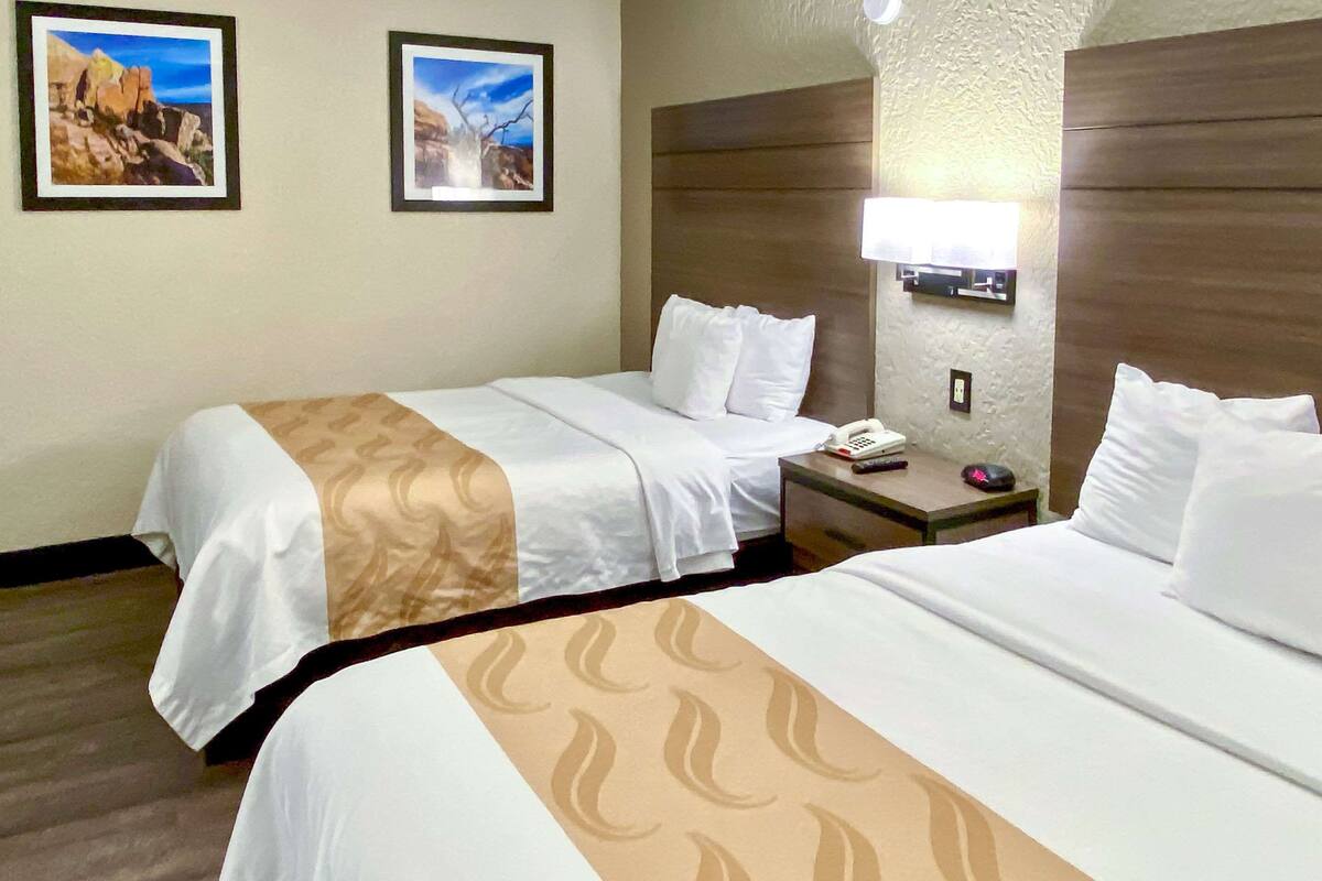 A hotel room with two beds, a nightstand, a lamp, and two framed pictures on the wall.