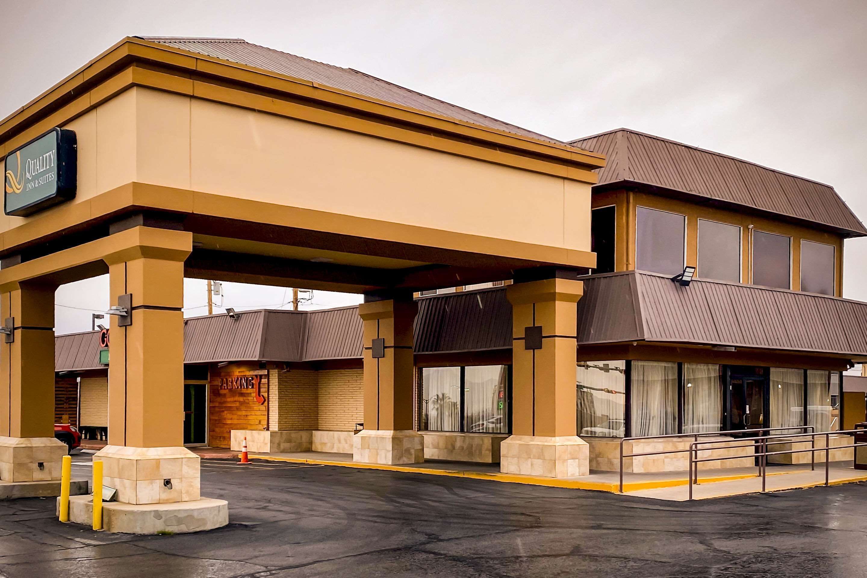 A hotel with a large sign, a covered parking area, and a building with large windows.
