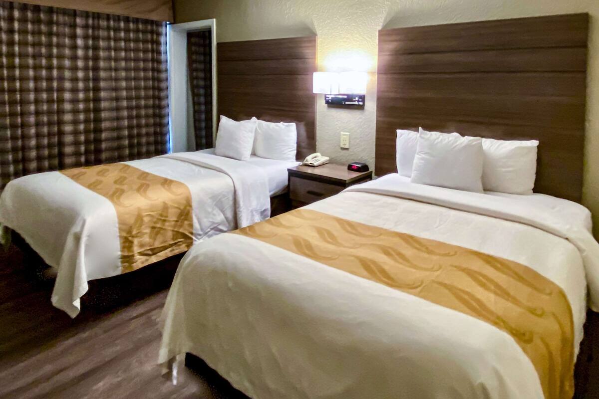 A hotel room with two beds, a nightstand with a lamp, and a check-in counter.