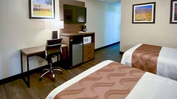 A hotel room with a desk, a refrigerator, a microwave, a chair, and two beds with patterned bedspreads.