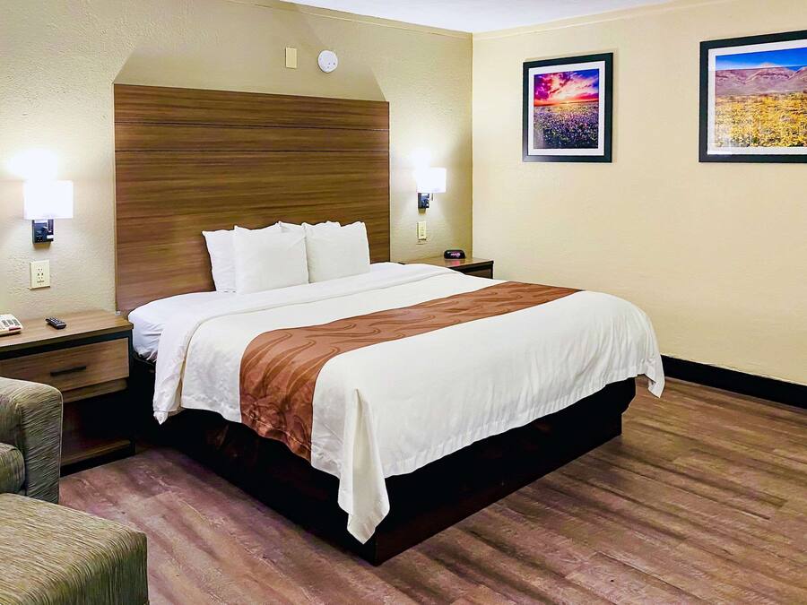 A hotel room with a large bed, bedside tables, a chair, and two wall-mounted lamps.