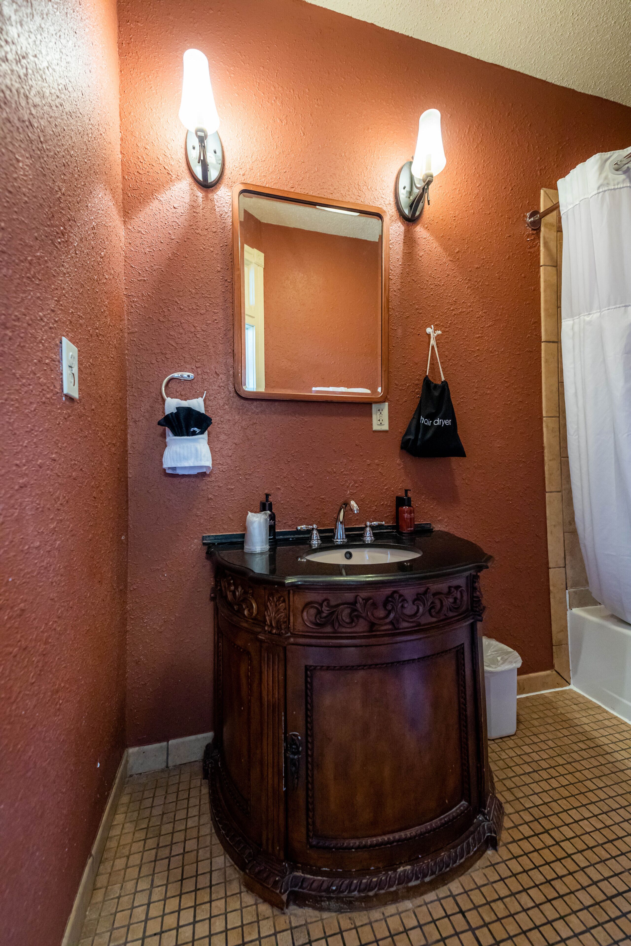 A bathroom with a wooden vanity, a mirror, two wall-mounted lights, a towel rack, and a shower curtain.
