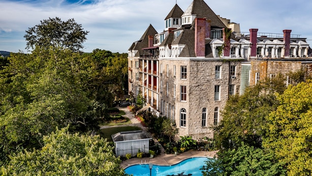 A large stone building with multiple towers and a swimming pool surrounded by lush greenery. - The Crescent Hotel and Spa (Eureka Springs)