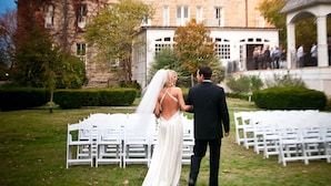 A couple walking down a grassy aisle in front of a large, historic building with multiple chimneys and a tower. - The Crescent Hotel and Spa (Eureka Springs)