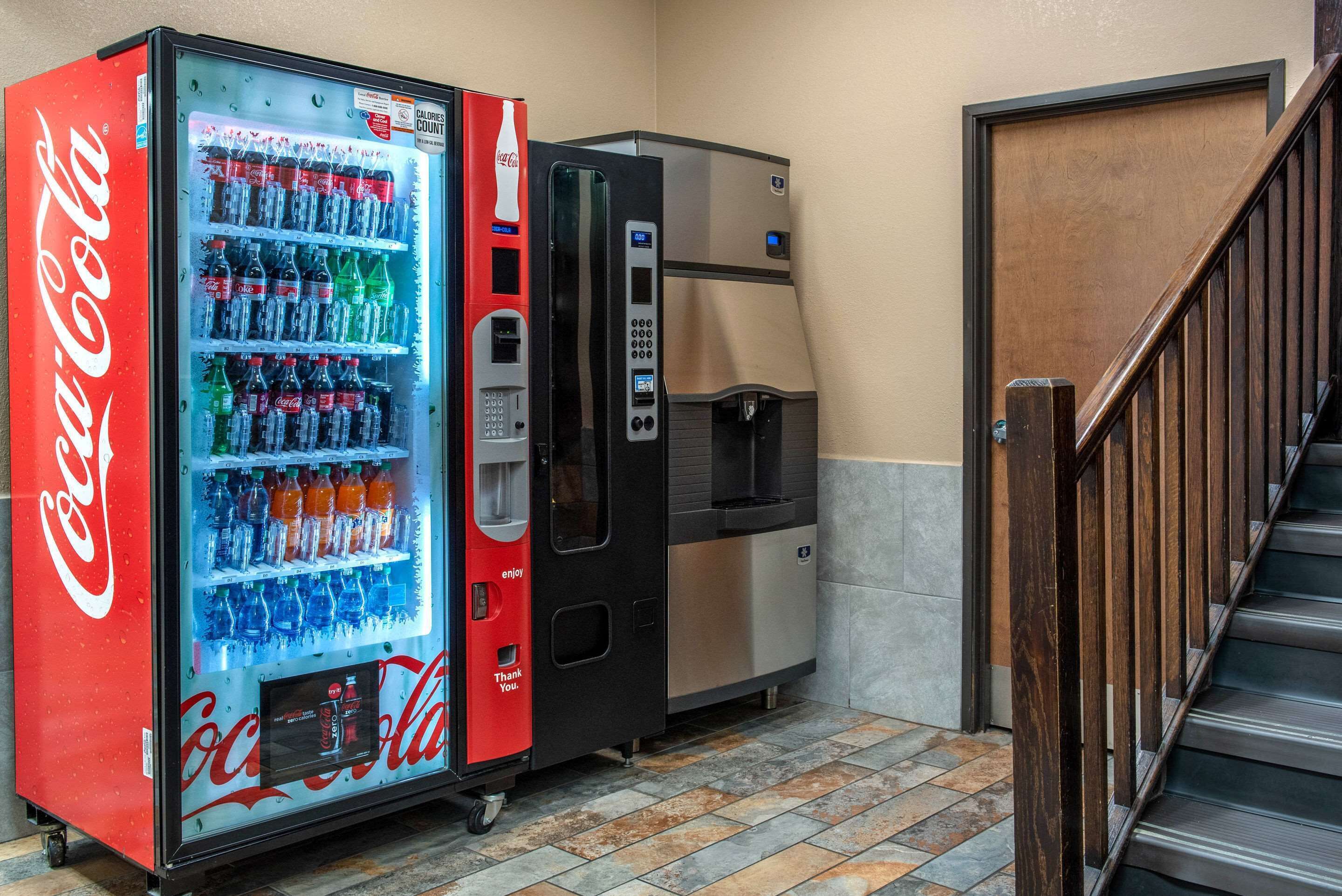 Una máquina expendedora de Coca-Cola y un dispensador de agua junto a una escalera.