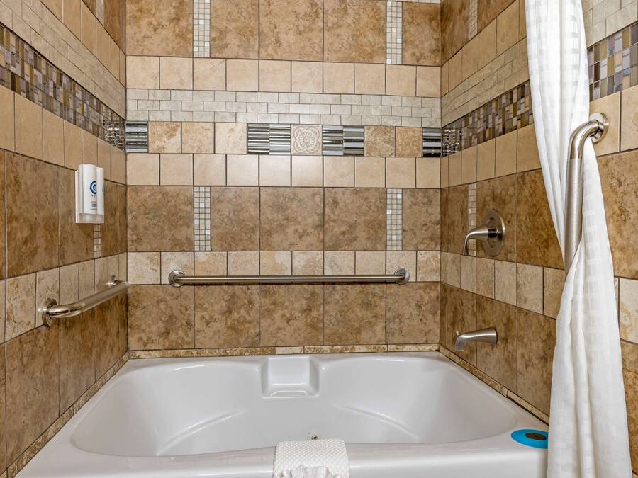 A bathroom with a bathtub, grab bars, and a shower curtain.