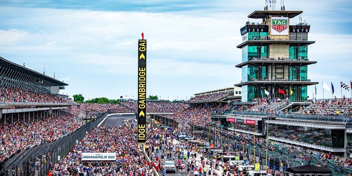 A crowded racing event with a large audience, a prominent gainbridge sign, and a TAG Heuer clock tower.