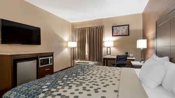 Quarto de hotel com uma cama, televisão de tela plana, escrivaninha com cadeira, micro-ondas e geladeira.