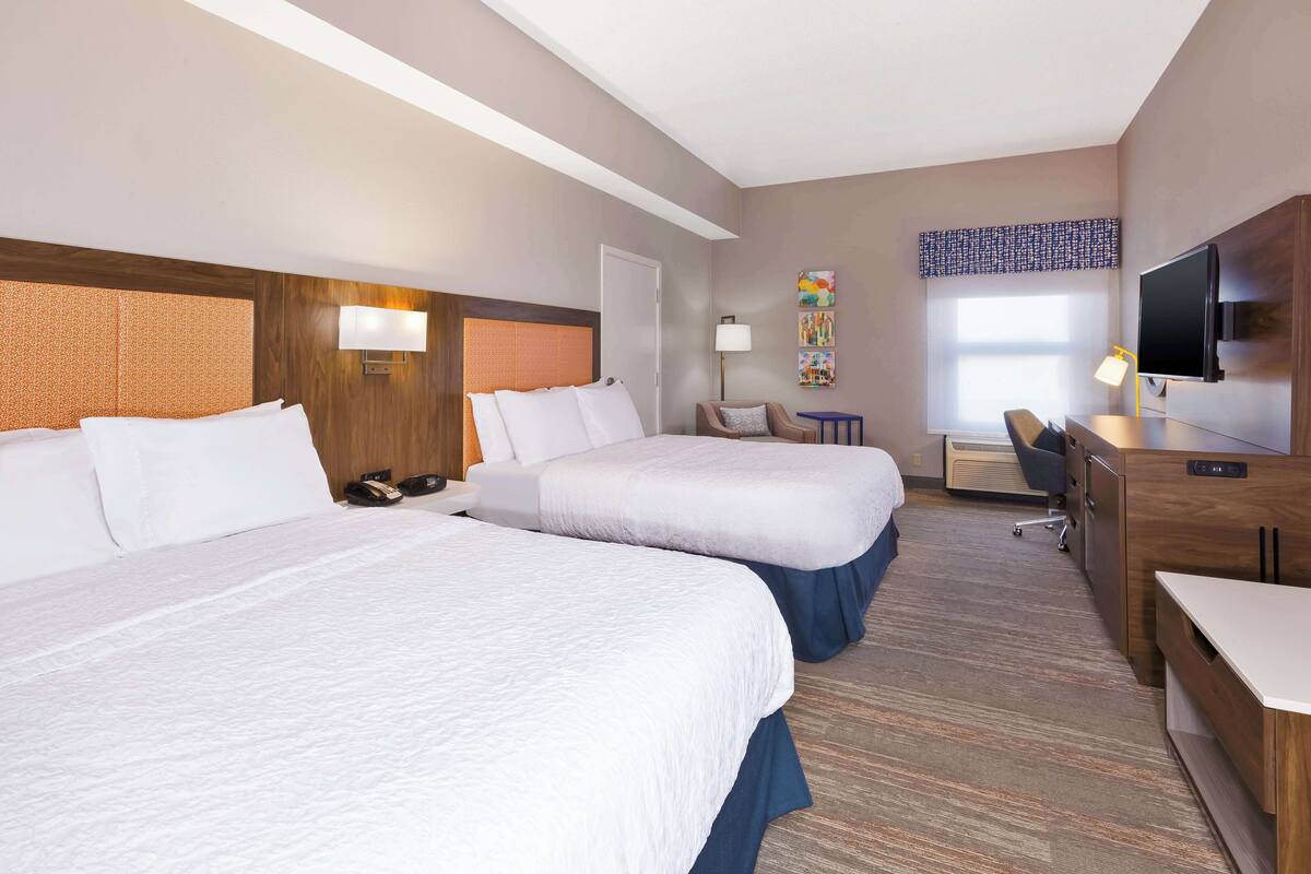A hotel room with two beds, a desk, a chair, a TV, and a window with a view.