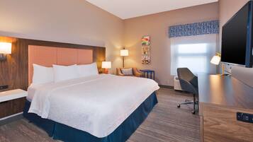A hotel room with a large bed, bedside tables, a desk, a chair, a flat-screen TV, and a window with a view.