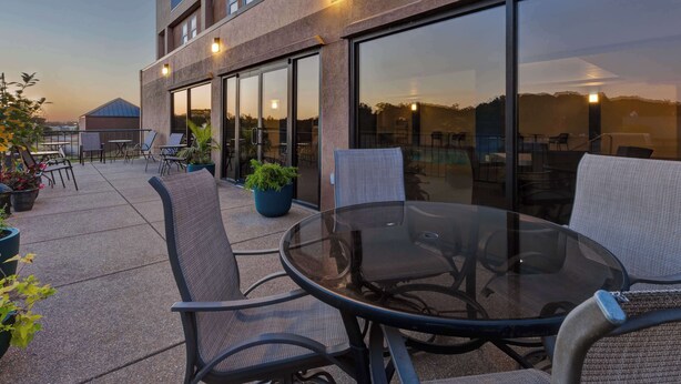 An outdoor patio area with a glass table and chairs, potted plants, and a building with large windows. - Hampton Inn Princeton (Princeton)