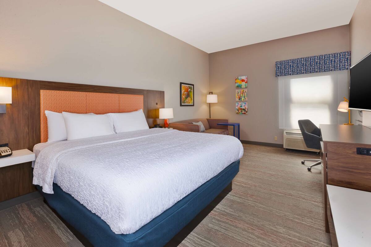 A hotel room with a large bed, a desk, a chair, and a TV.