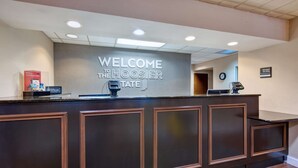 A reception desk with a "WELCOME TO THE HOOSIER STATE" sign, a clock, and a "Manager On Duty" sign. - Hampton Inn Princeton (Princeton)