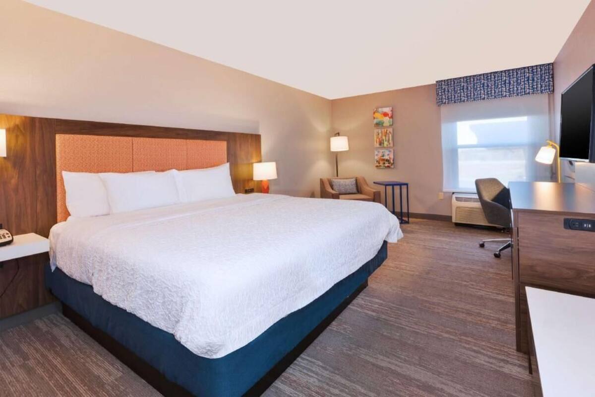 A hotel room with a large bed, bedside lamps, a desk with a chair, a television, and a window with a view.