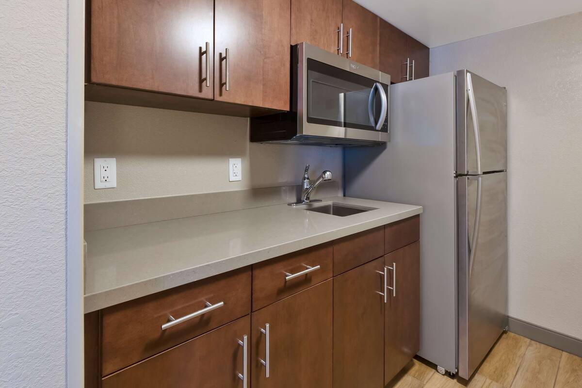 A kitchen with wooden cabinets, a stainless steel refrigerator, a microwave, and a sink.