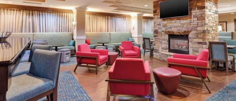 A hotel lobby with seating areas, a fireplace, and a television mounted on a stone wall.