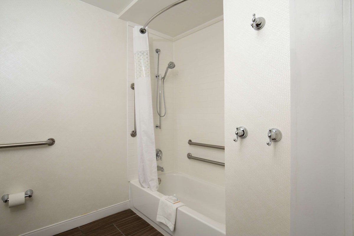 A bathroom with a bathtub, a shower, and a toilet. It includes grab bars and a towel rack.
