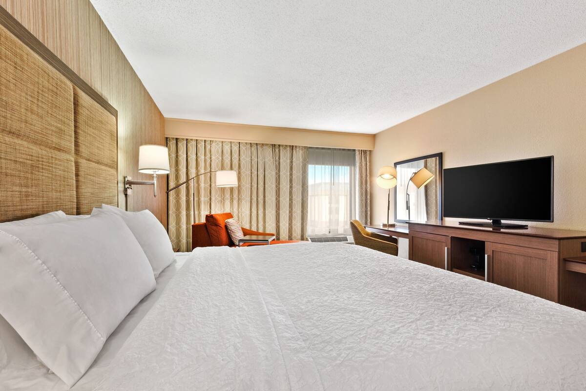 A hotel room with a large bed, a desk with a television, and a chair.