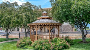 A gazebo with a stone base and a wooden upper structure, surrounded by a garden with pink flowers and trees. - Hampton Inn Collinsville (Collinsville)