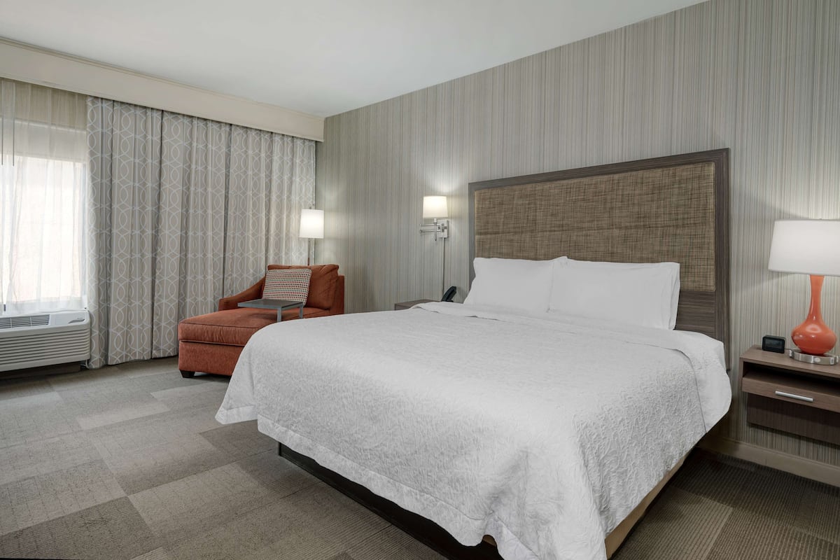 A hotel room with a large bed, a chair, a nightstand, and a lamp.