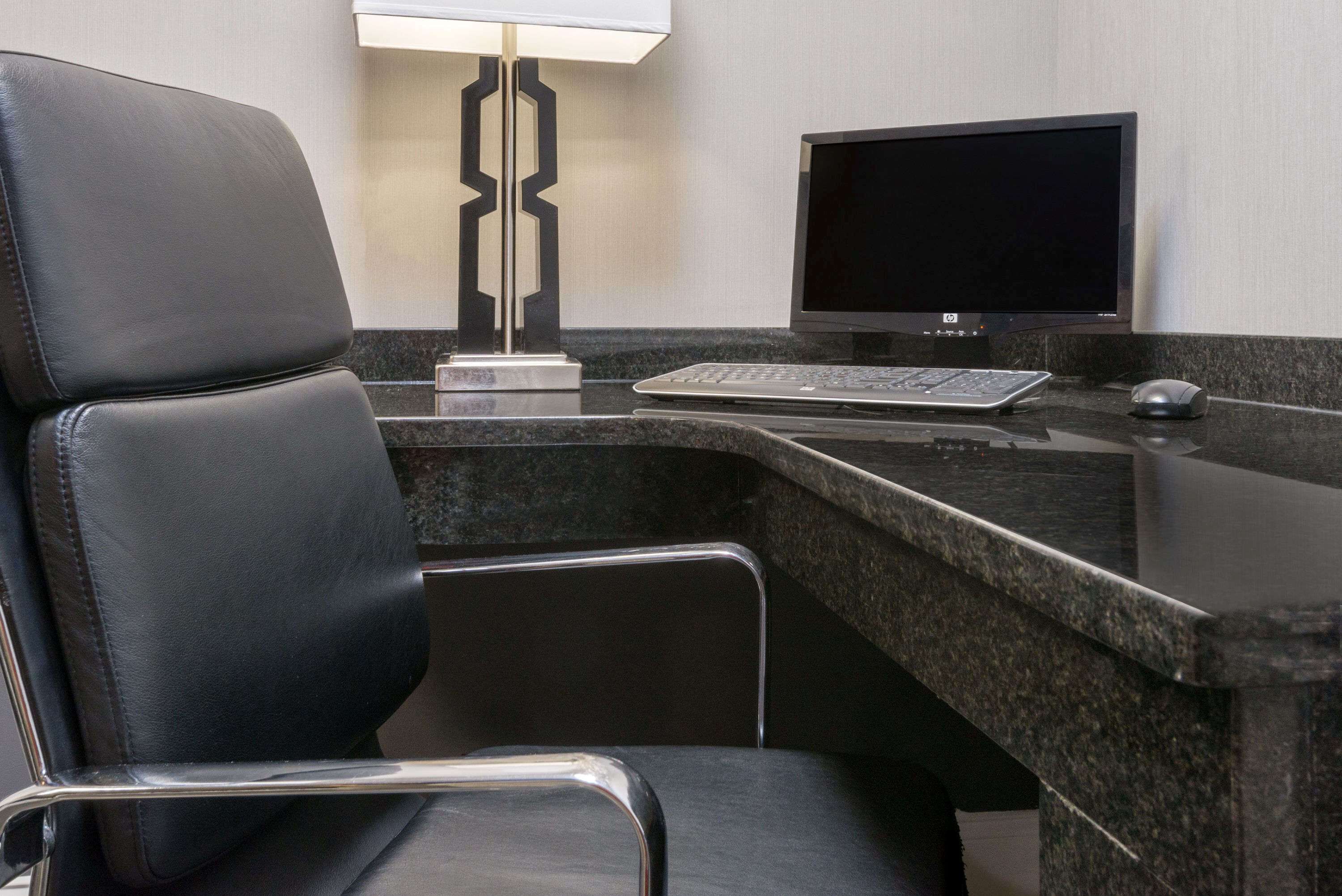 A modern office chair, a desktop computer, and a desk lamp in a hotel room.